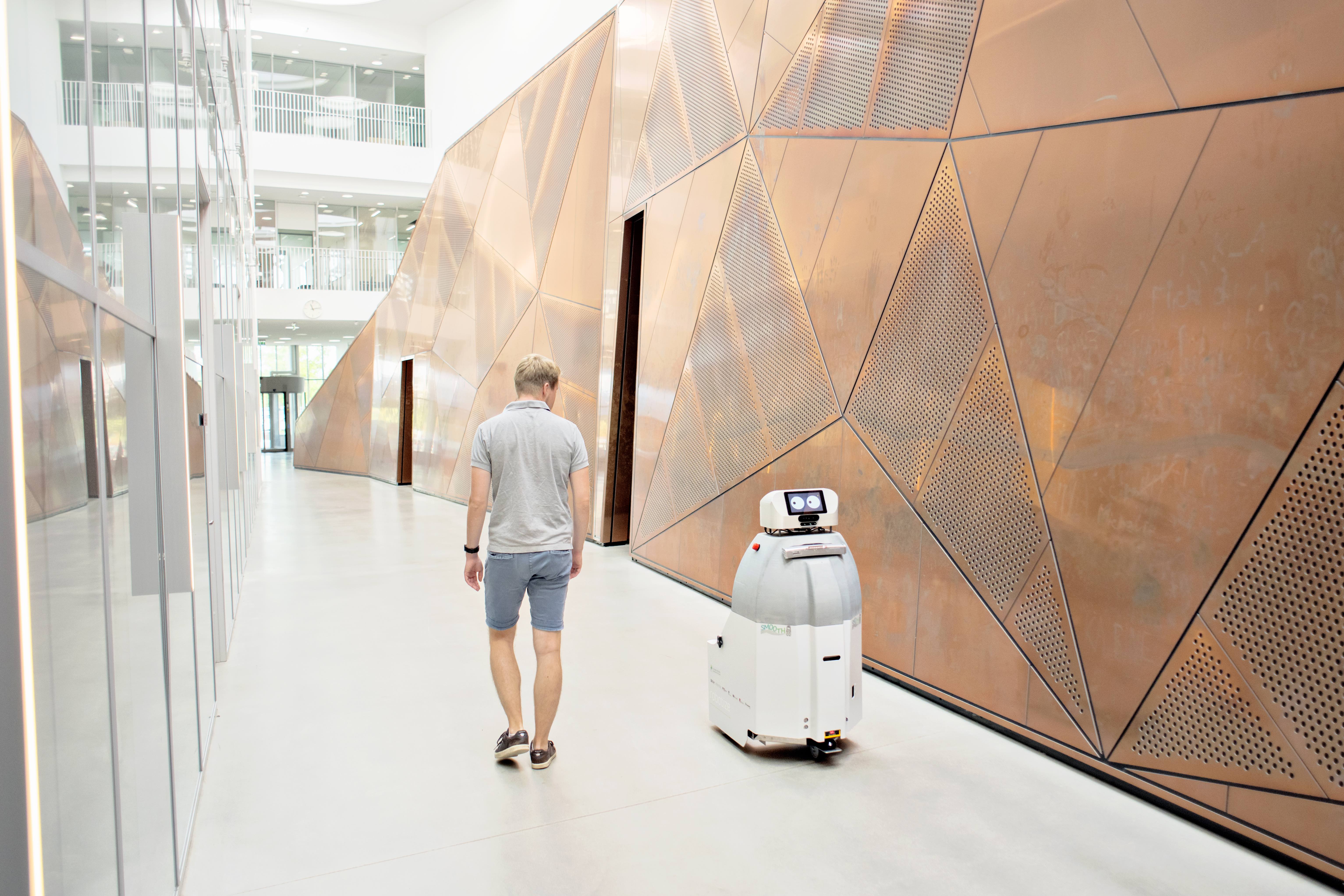 En man går i en korridor och bredvid sig har han en robot